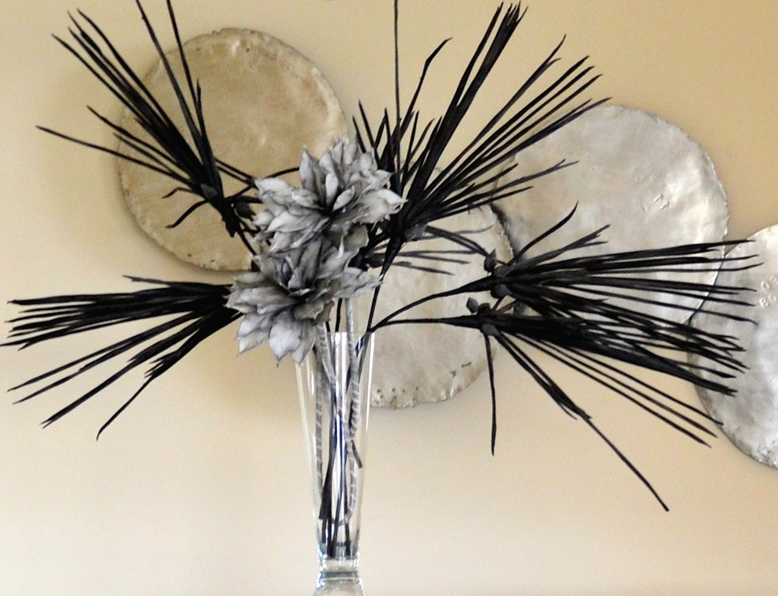 Flower vase wallpaper — silk grey blooms with black spiky stems in a glass vase against circular wall sculptures